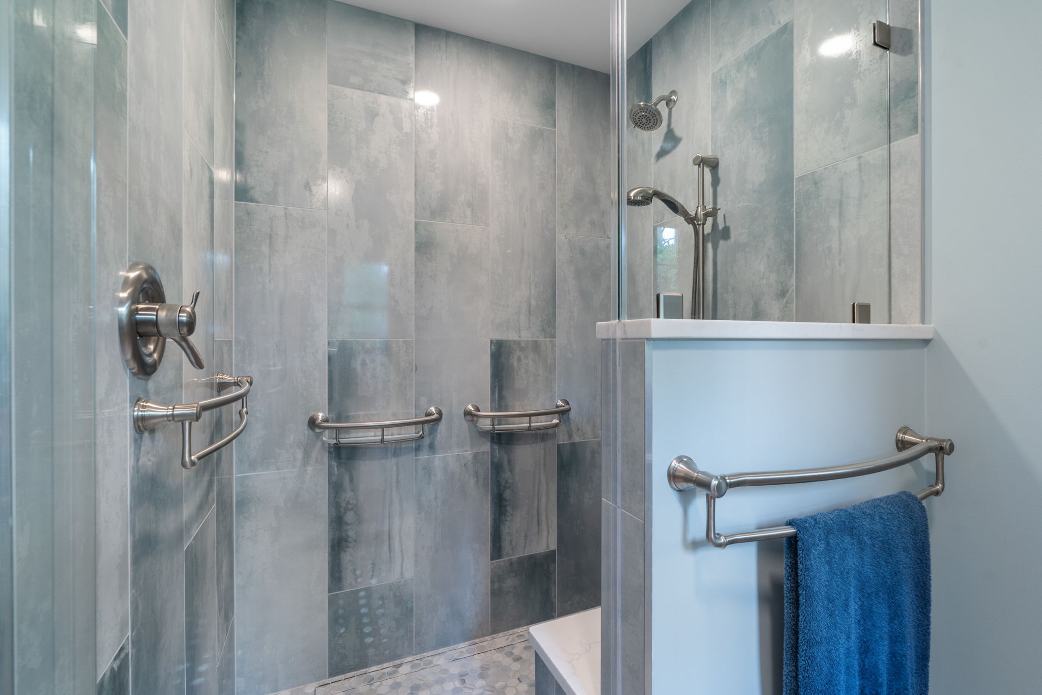 Modern walk-in shower with Ora Beach blue wall tile, hex mosaic shower floor, and integrated brushed nickel grab bars.