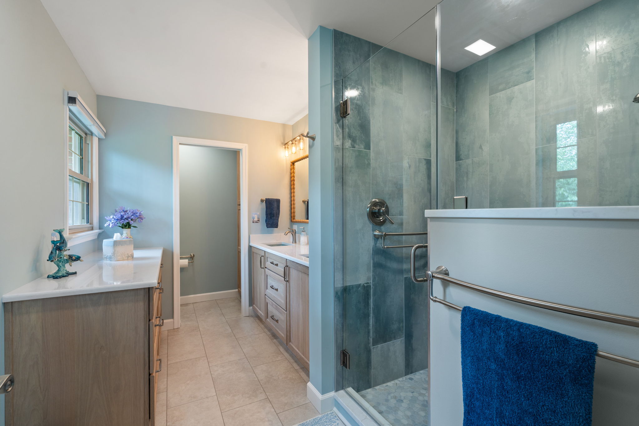 Remodeled primary bathroom in Virginia Beach featuring blue shower tile, custom Shiloh cabinetry, quartz countertops, and aging-in-place grab bars.