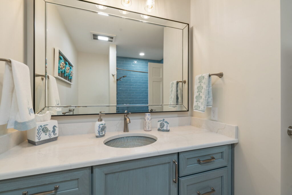 Updated hall bathroom featuring blue vanity, quartz countertop, statement sink, and coastal-inspired tile selections